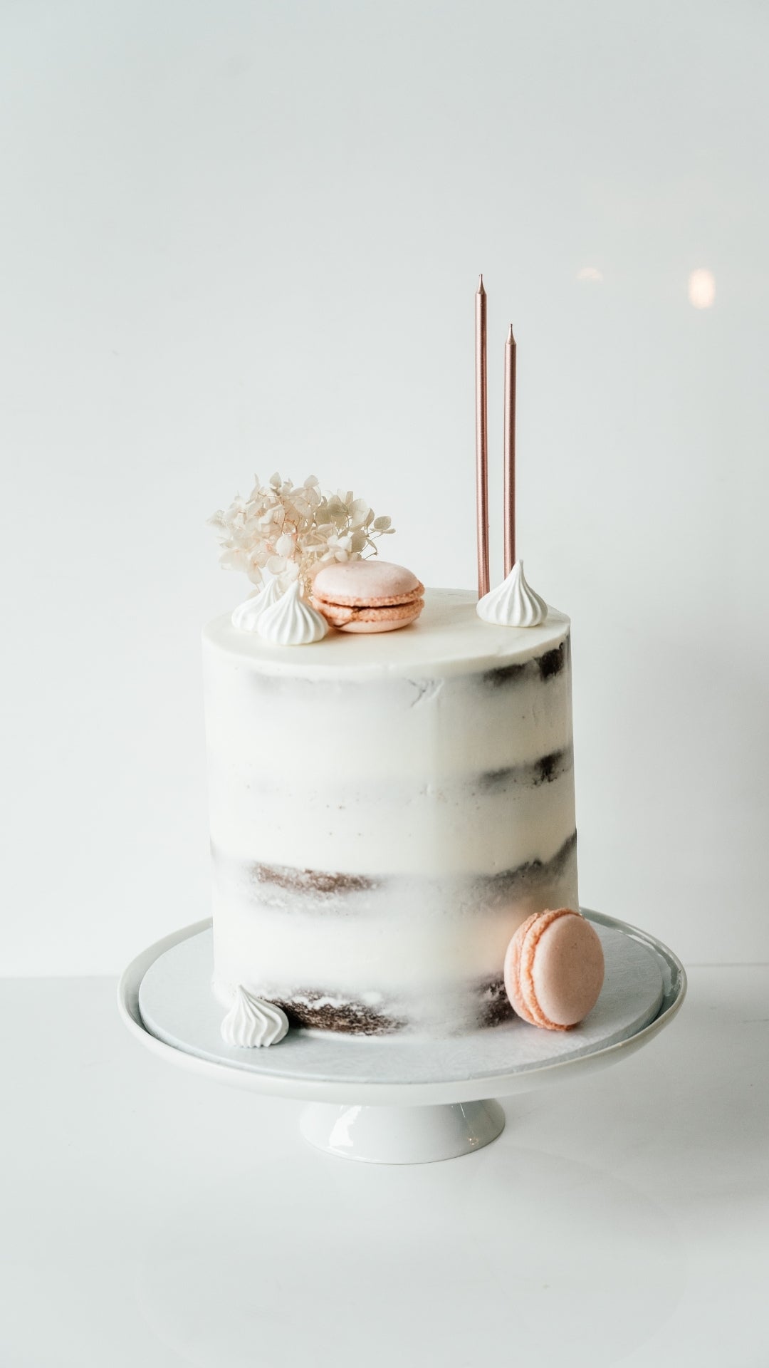 Small marble cake with candles and macarons on a white background